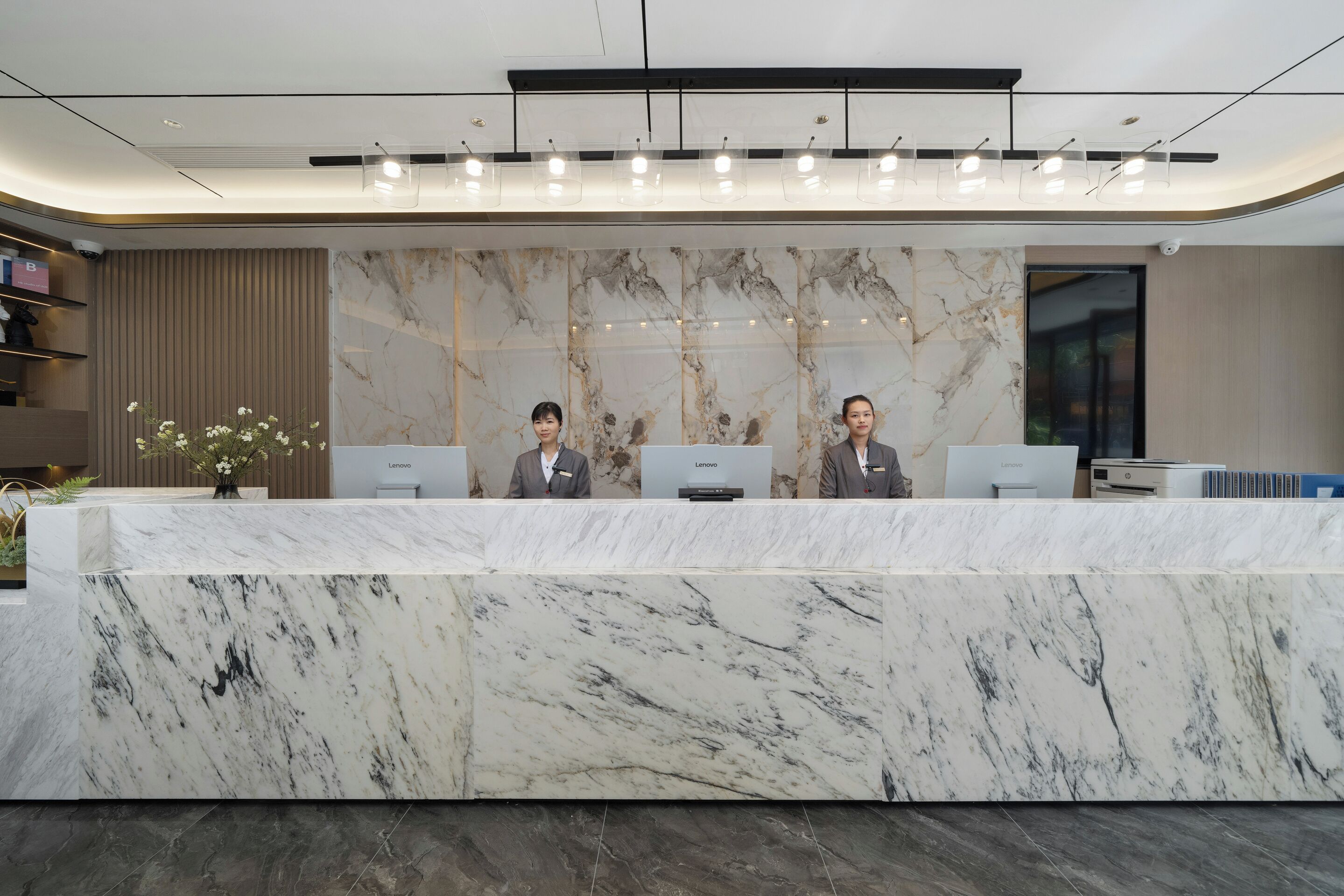 A reception desk with a marble top, two staff members, and a Lenovo computer.