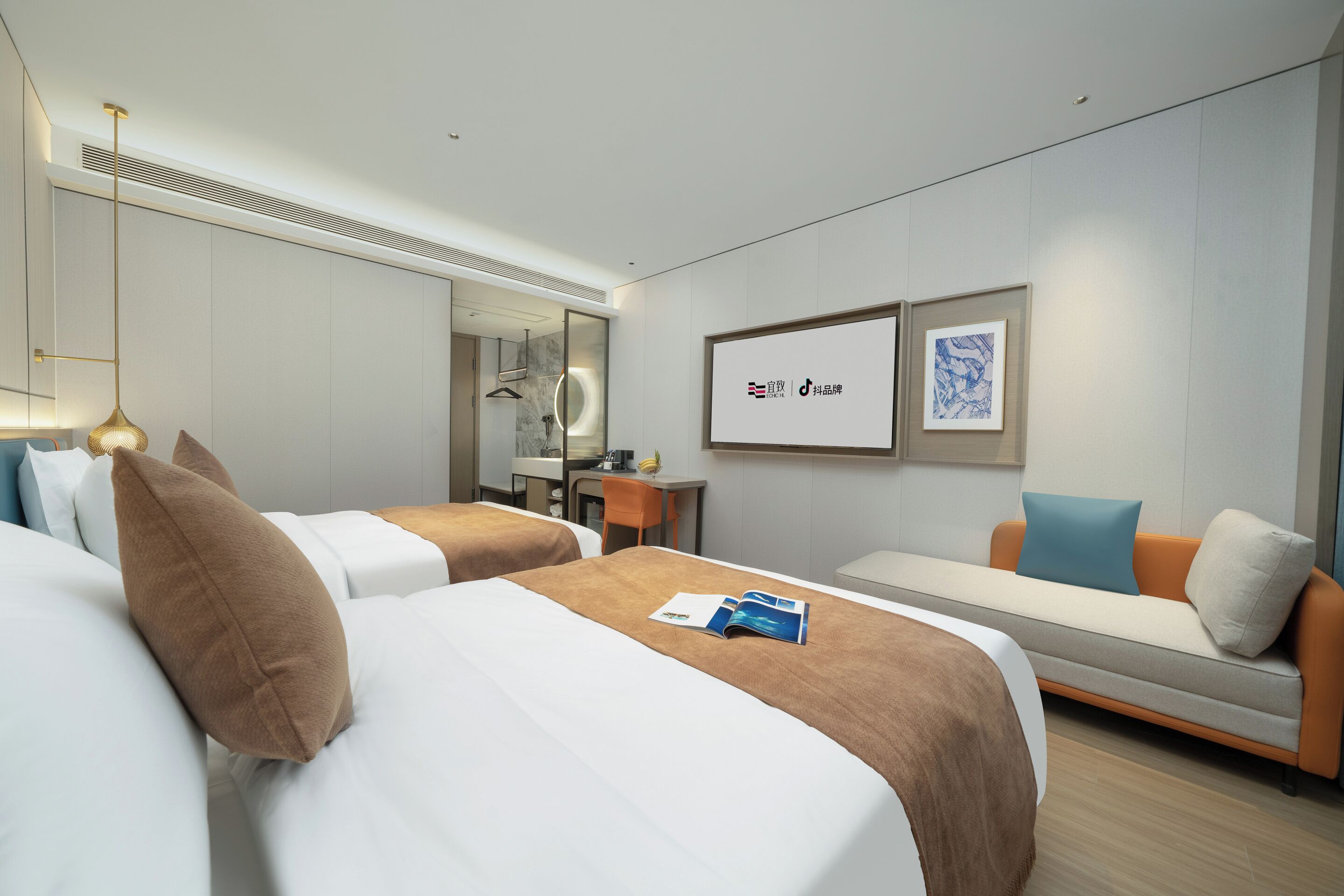 A hotel room with two beds, a sofa, a desk, and a mirror. There are framed pictures on the wall and a hanging light fixture.