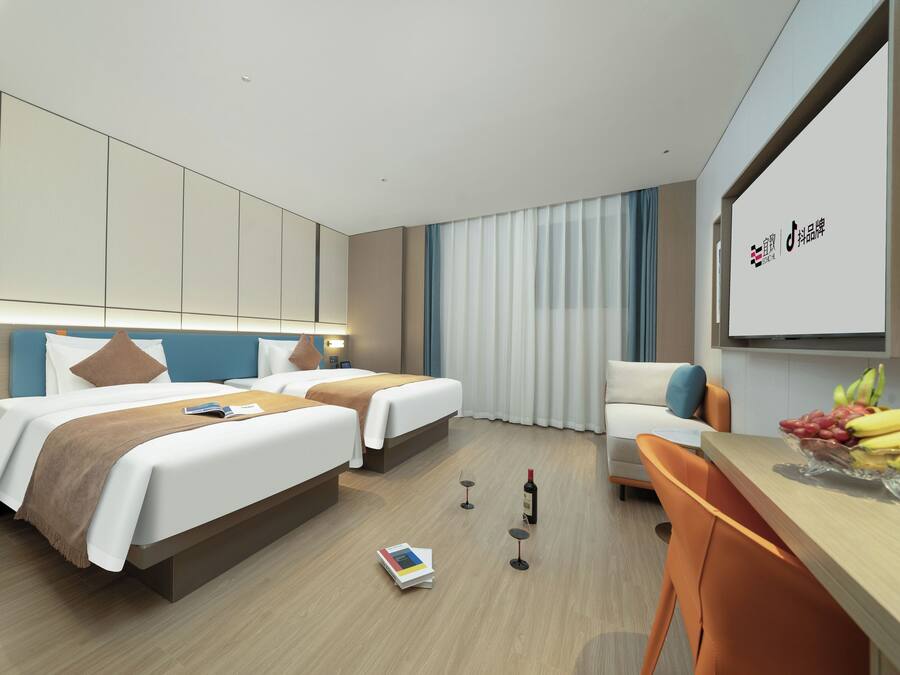A modern hotel room with two beds, a desk, a chair, and a dining table with fruit.