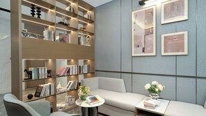 A modern reading area with a sofa, a small table with a book, and a bookshelf filled with books and decorative items. - YiZhi HotelShangxiajiu Pedestrian Stree (Guangzhou)
