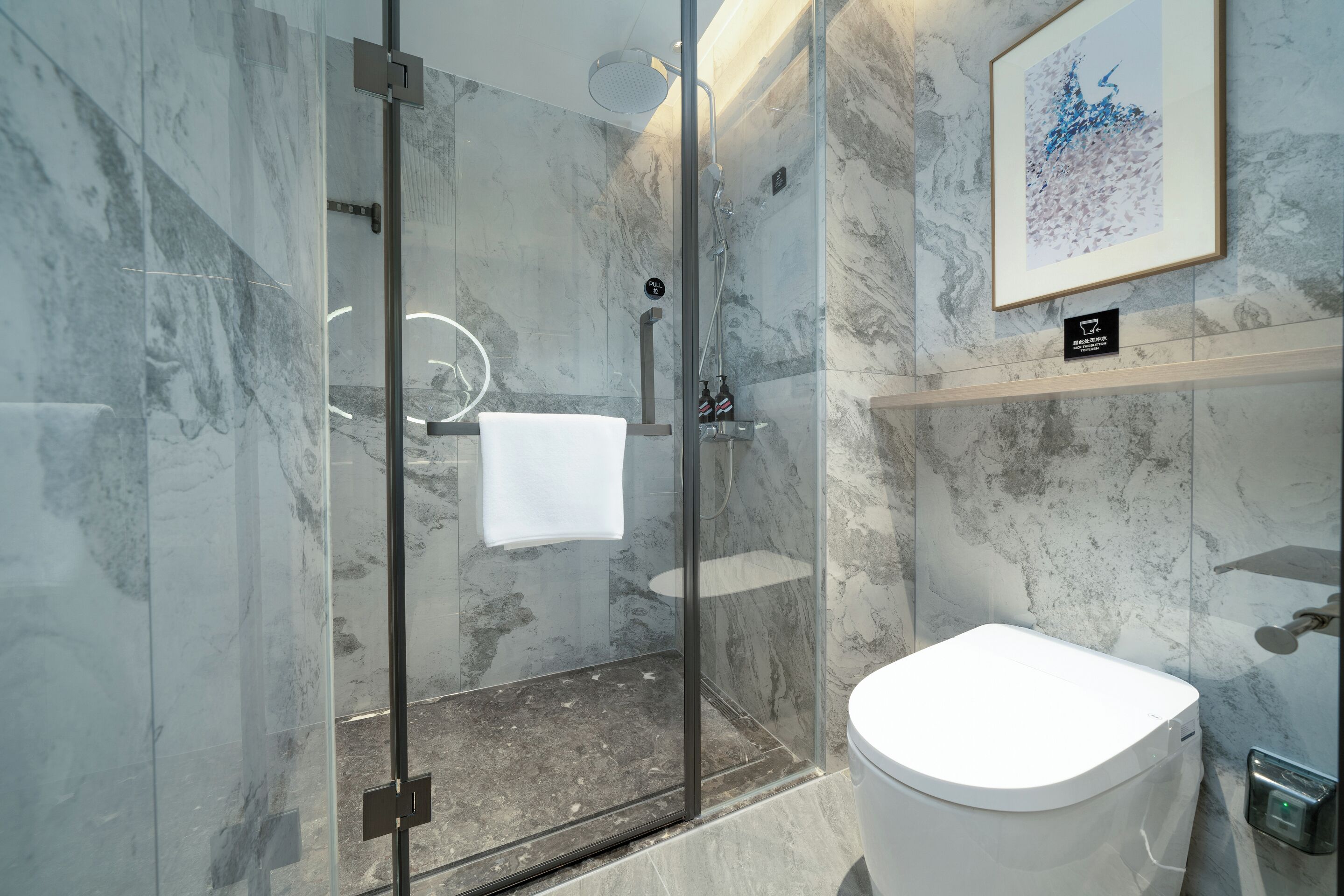 Un baño moderno con ducha envuelta en vidrio, inodoro blanco y pared de mármol.