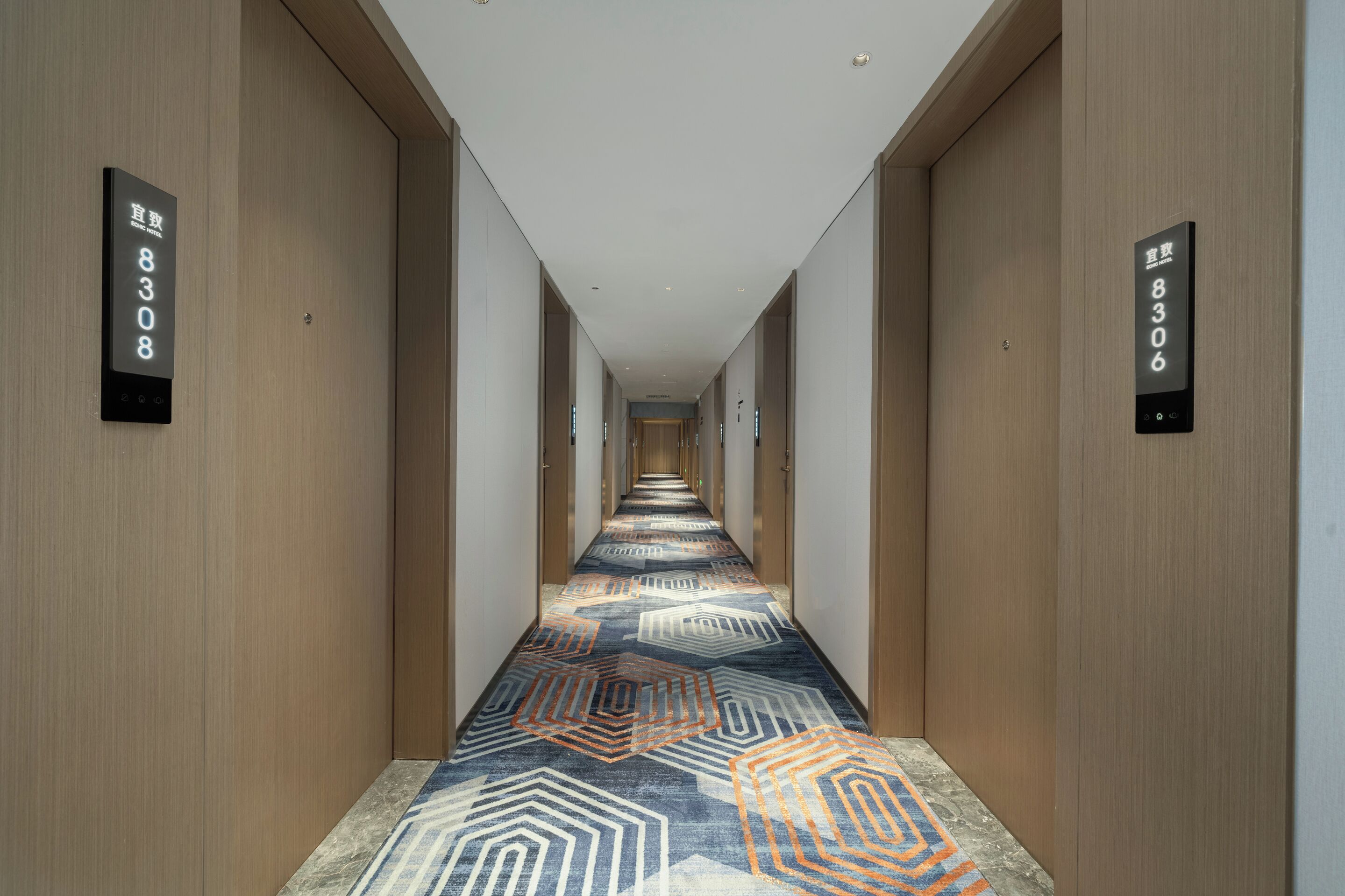 A hotel hallway with a patterned carpet, wooden walls, and numbered signs indicating room numbers 8308 and 8306.