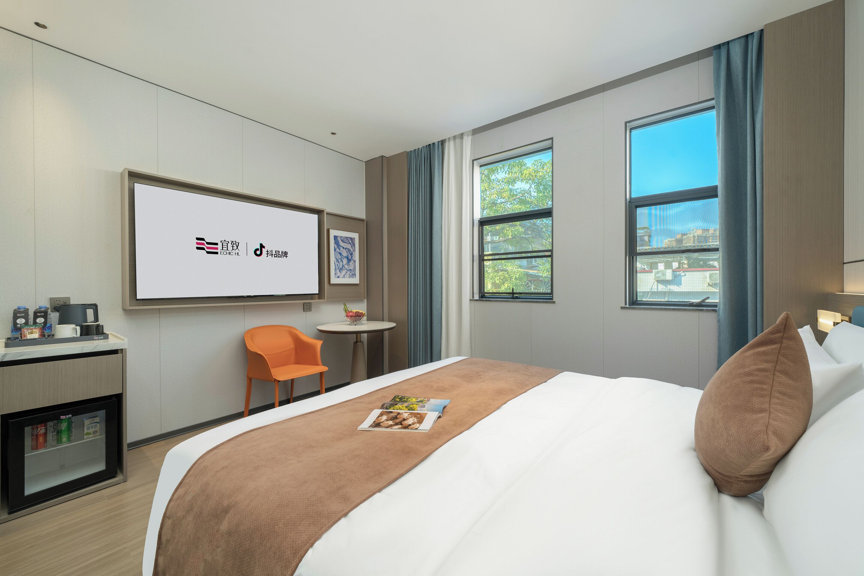Habitación de hotel con cama, escritorio con computadora, silla, mesita con frutero y ventana grande.