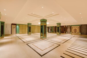 Un vestíbulo amplio con techo alto, columnas verdes y suelo con diseño.