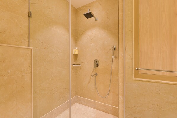 Un espace douche clos par des parois de verre, doté d’un pommeau de douche à main et d’un robinet mural.