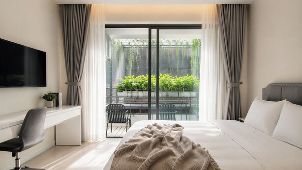 A modern hotel room with a bed, desk, chair, and a balcony with plants. - Centraltique Veranda Living (Hanoi)