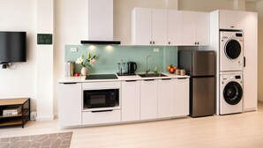 A modern kitchen with white cabinets, a built-in microwave, a stainless steel refrigerator, and a washing machine. - Centraltique Veranda Living (Hanoi)