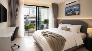 A hotel room with a bed, desk, chair, and a balcony with a view of buildings. - Centraltique Veranda Living (Hanoi)