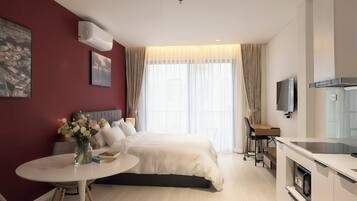 A modern hotel room with a bed, a desk, a TV, and a kitchenette.