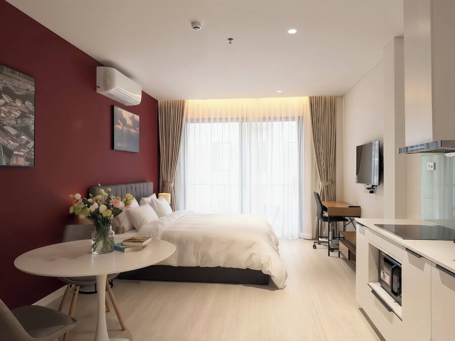A modern hotel room with a bed, a desk, a TV, and a kitchenette.