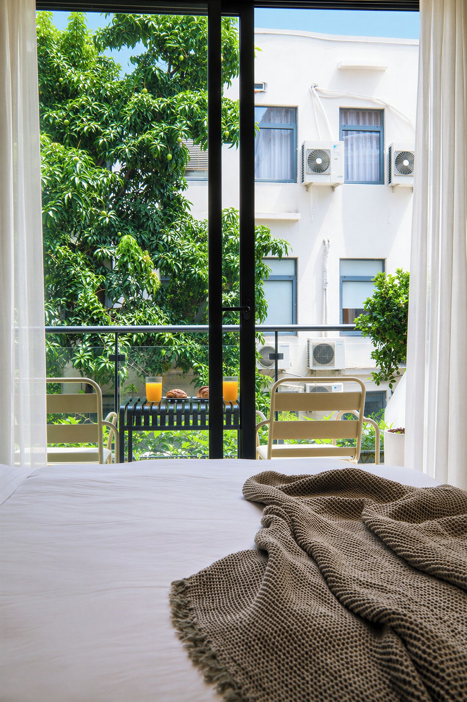 Een balkon met uitzicht op een gebouw, een tafel met stoelen en een bed met dekbed.