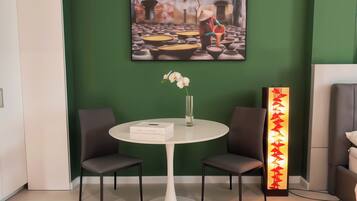 A modern room with a green wall, a round white table with two chairs, a vase with flowers, and a framed picture above the table.