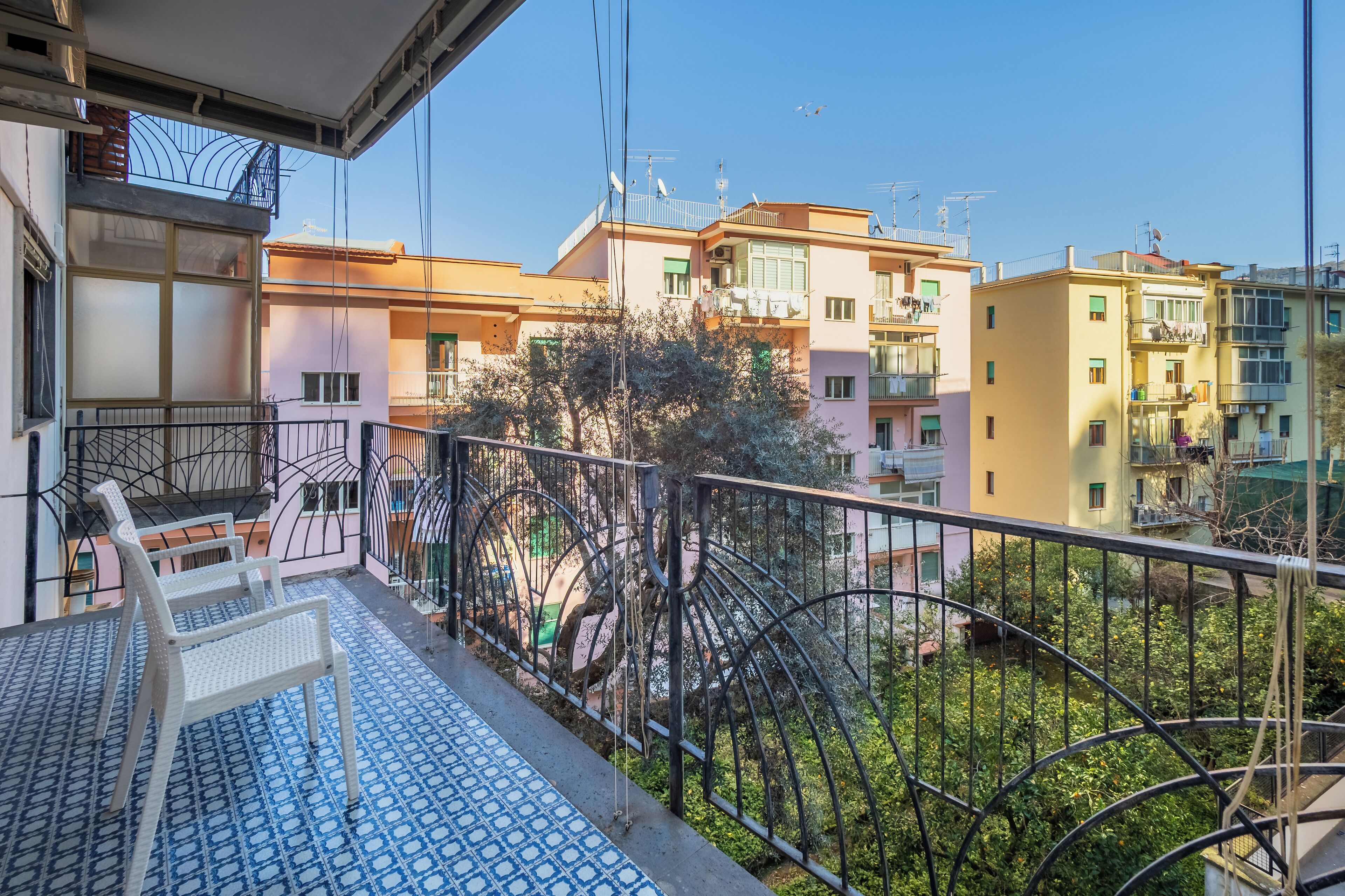 A balcony with a patterned floor, a white chair, and a view of neighboring buildings.