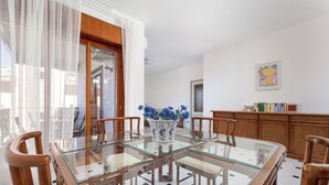 A dining area with a glass-top table, wooden chairs, a vase with flowers, and a bookshelf. - Capo Sereno (Sorrento)