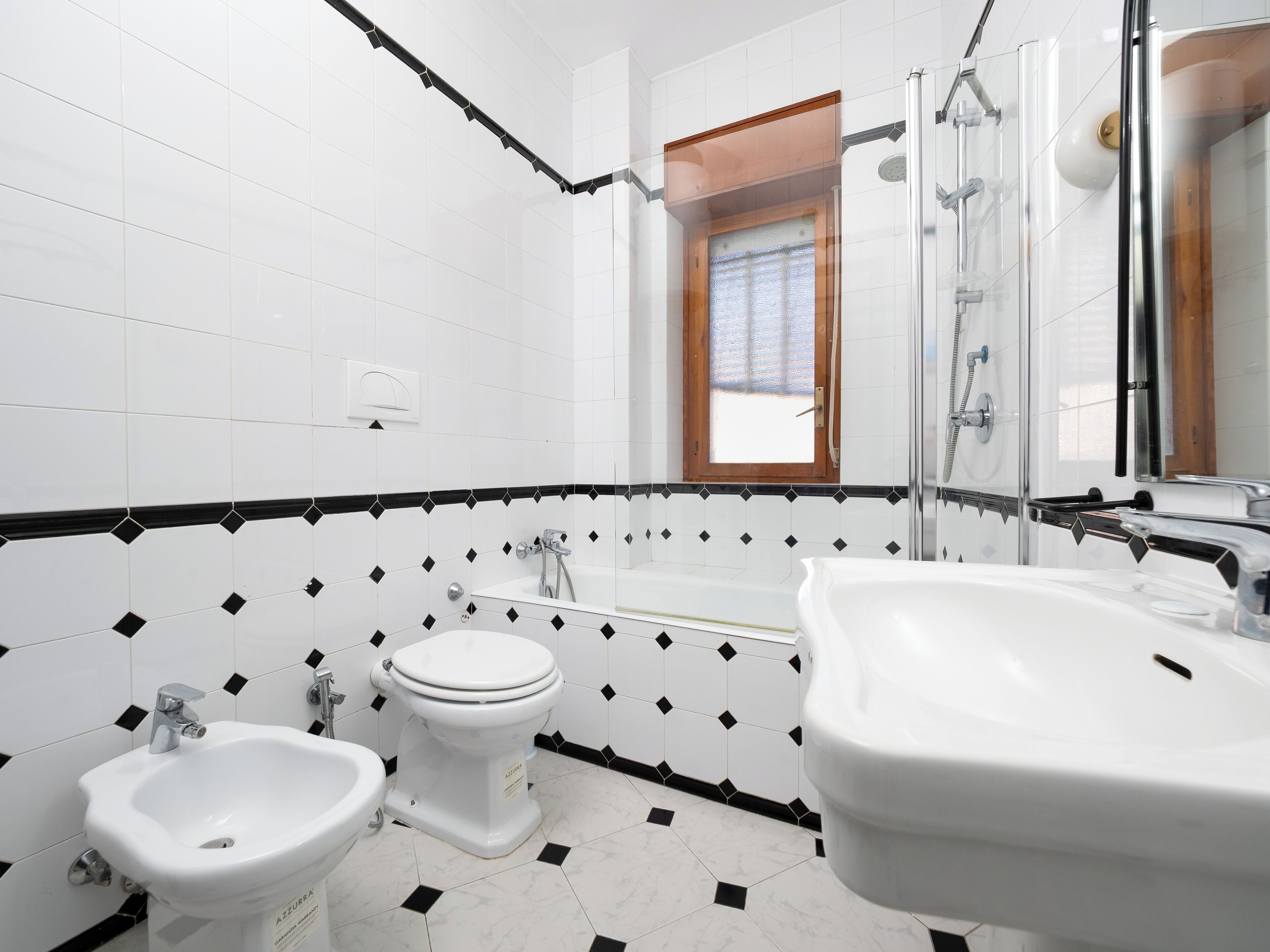 A modern bathroom with a white and black tiled floor, a toilet, a bidet, and a bathtub.