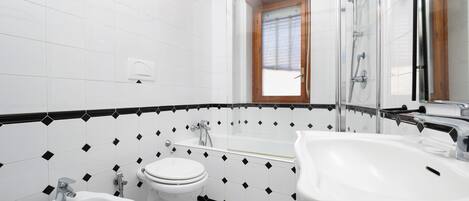 A modern bathroom with a white and black tiled floor, a toilet, a bidet, and a bathtub.