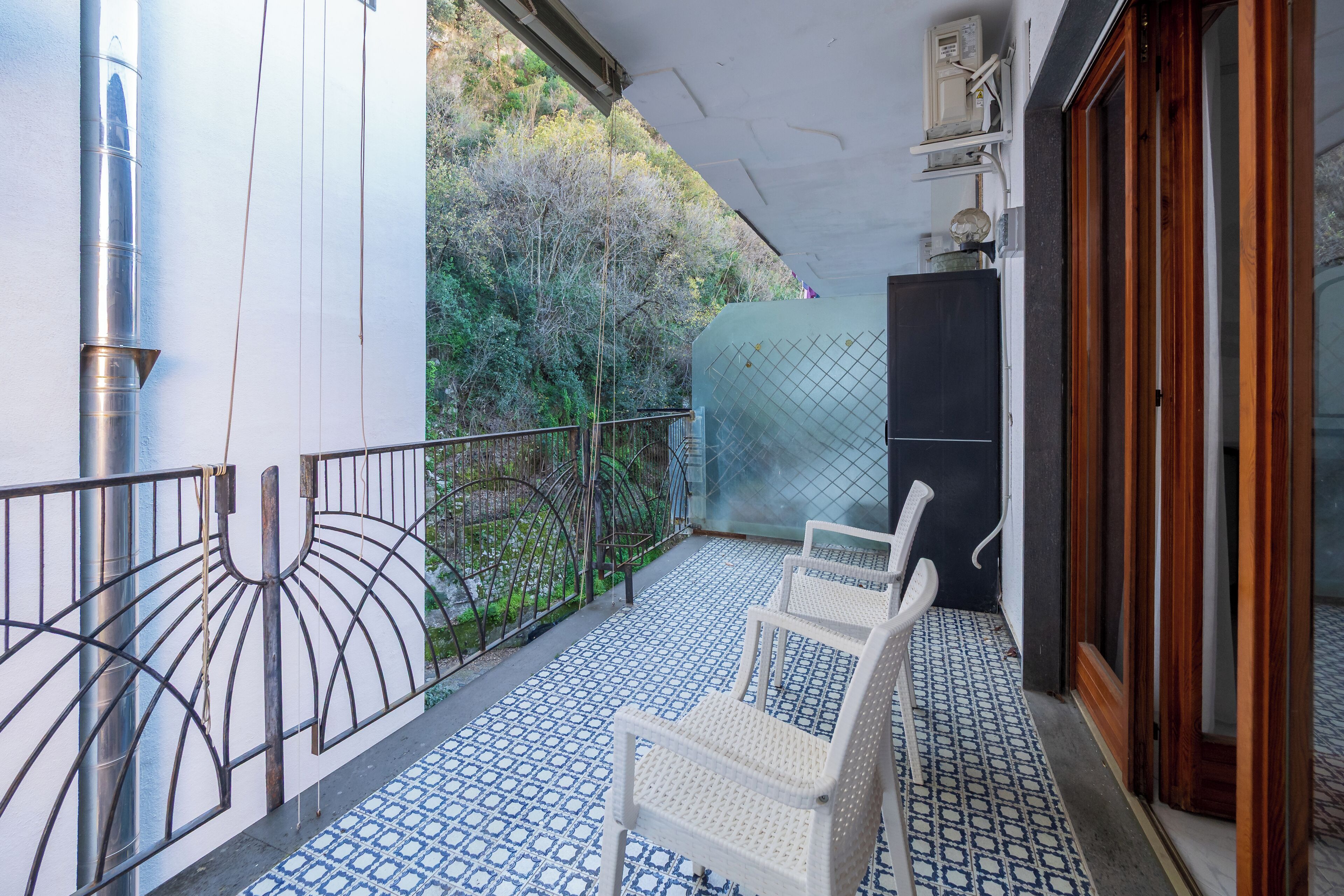 A balcony with white wicker chairs, a metal railing, and a patterned floor.