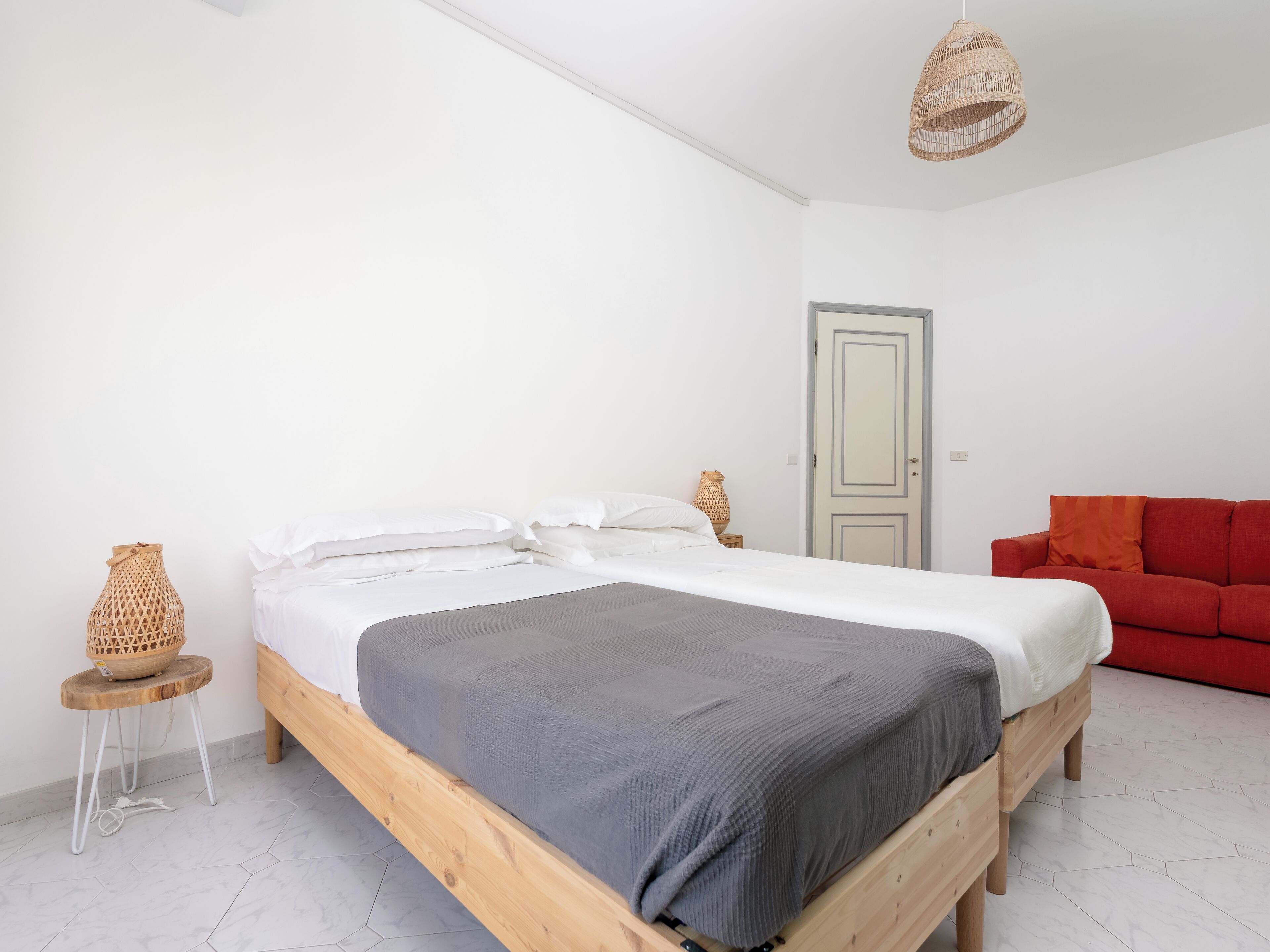 A bedroom with a wooden bed, a small side table, a red sofa, and a woven lamp.