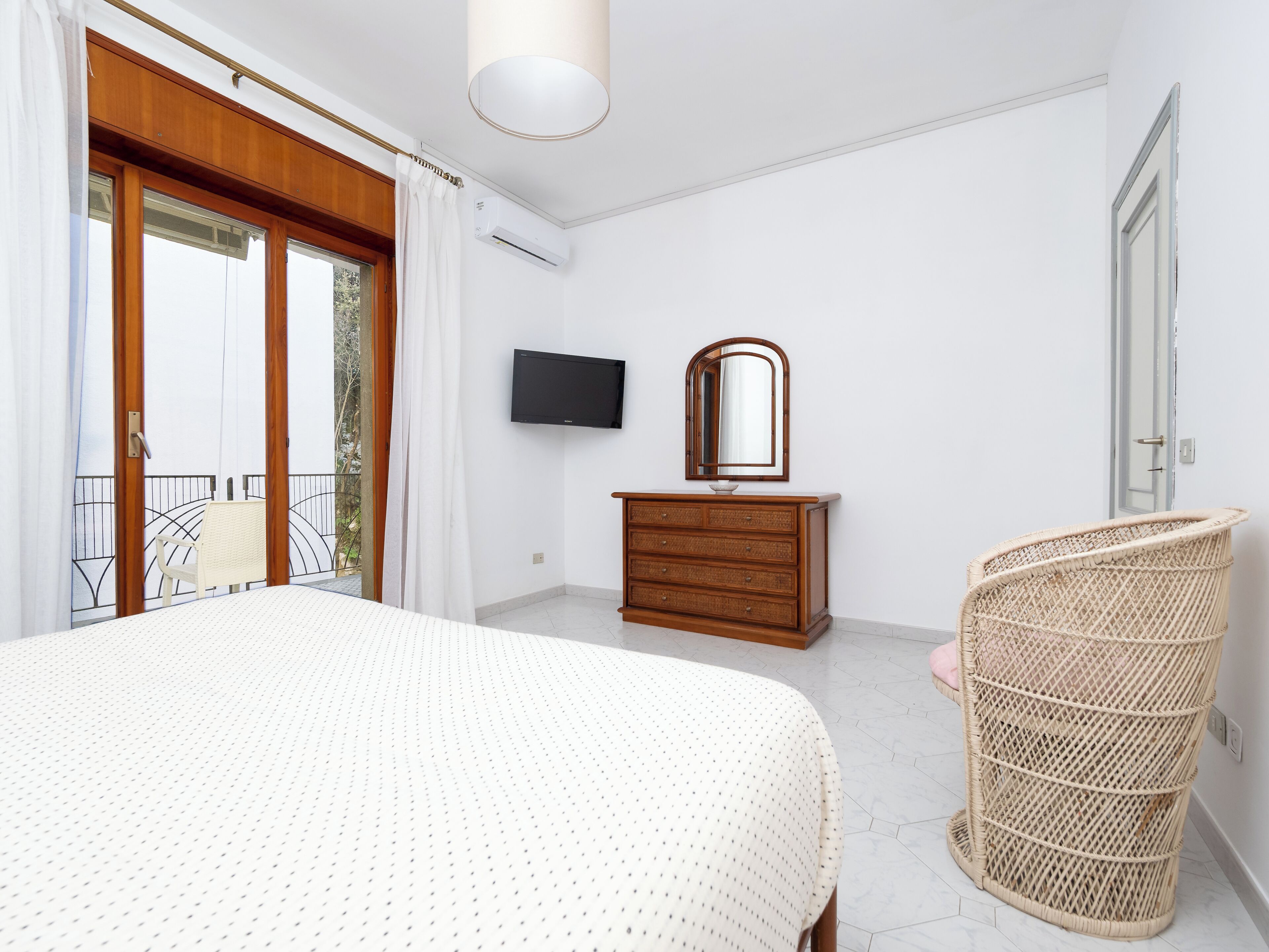 Een slaapkamer met een bed, een kaptafel, een televisie en een rieten stoel.