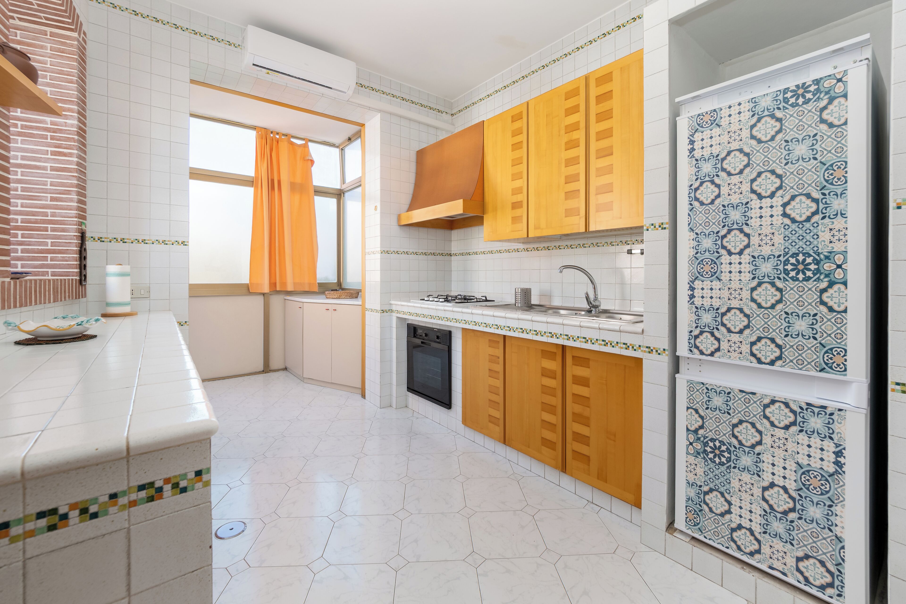 A kitchen with white hexagonal tiles, wooden cabinets, a gas stove, and a patterned backsplash.