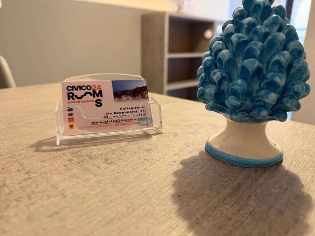 Un letrero de plástico transparente con texto y una dirección web, colocado sobre una mesa junto a un objeto decorativo azul.