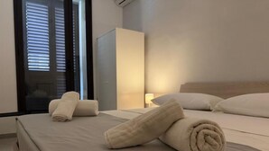 A hotel room with a bed, two rolled towels, a nightstand, and a window with blinds. - Comfort, style and views: your perfect stay at Civico24rooms (Caltagirone)