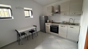 A compact kitchen with a white countertop, stainless steel appliances, and a small dining area with two chairs. - An elegant retreat overlooking the city of mosaics (Caltagirone)
