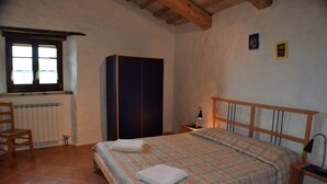 A bedroom with a bed, a chair, a wardrobe, a nightstand with a lamp, and a window with curtains. - Agriturismo Alla Vecchia Quercia vacation apartment "Cagli" for 2 persons (Pergola (PU))