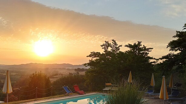 A swimming pool with lounge chairs and umbrellas, surrounded by a garden and a view of the sunset over hills. - Agriturismo Alla Vecchia Quercia vacation apartment "Cagli" for 2 persons (Pergola (PU))