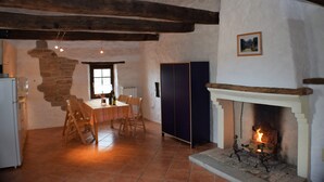 A rustic interior with exposed wooden beams, a fireplace, a dining area with a table and chairs, and a stone wall. - Agriturismo Alla Vecchia Quercia vacation apartment "Cagli" for 2 persons (Pergola (PU))