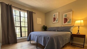 A bedroom with a bed, a nightstand, a lamp, and a window with curtains. - Stockbridge Home w/ Master Suite on the Main (Stockbridge)