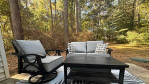 An outdoor seating area with a black table and two chairs, a patterned rug, and a backdrop of trees. - Stockbridge Home w/ Master Suite on the Main (Stockbridge)