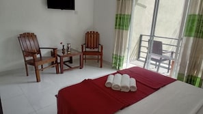 Habitación de hotel con una cama, dos sillas de madera, una mesita y un balcón con una silla.