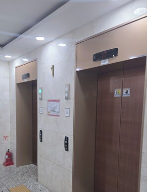 Un ascensor con pantalla digital, botones de emergencia y un extintor en el suelo.