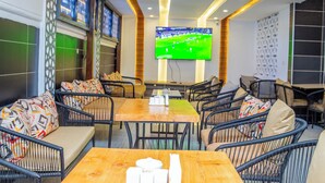 A restaurant with high tables and chairs, a large TV screen displaying a soccer match, and patterned cushions on the seating. - Sukoon Nyali Suites (Mombasa)