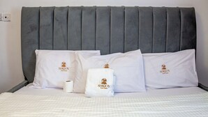 A neatly made bed with white linens and pillows, each featuring a logo and text. - Sukoon Nyali Suites (Mombasa)