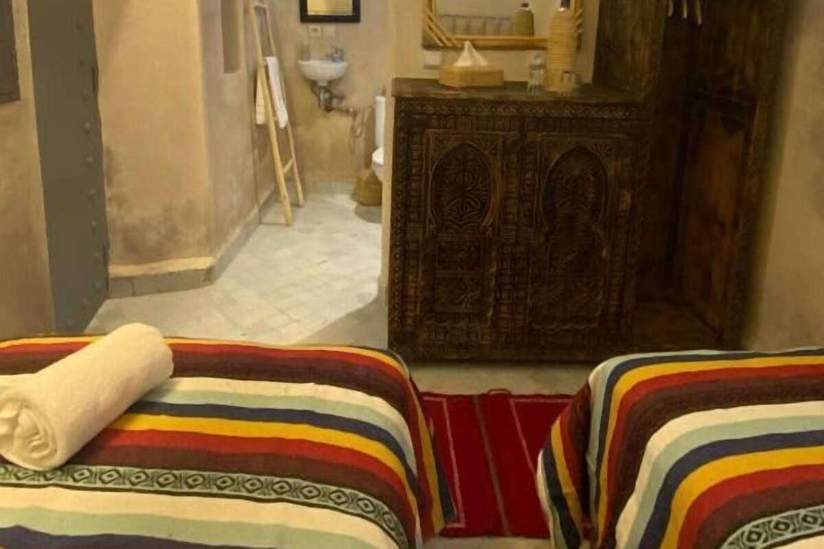Una camera d'albergo con due letti, un armadietto in legno, uno specchio e un bagno sullo sfondo.