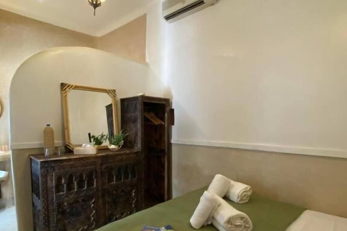 Una camera d'albergo con un letto, una cassettiera, uno specchio e un condizionatore d'aria.