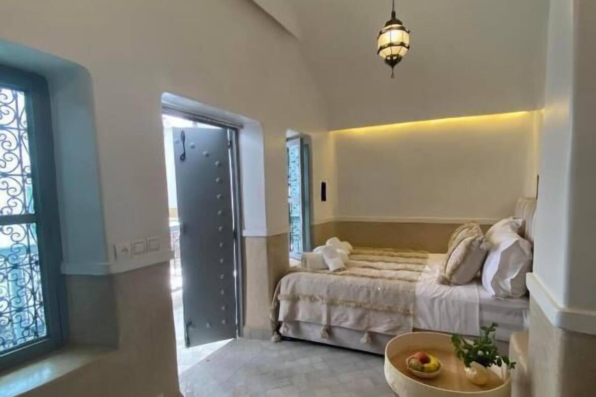 Una camera da letto con un letto, un comodino con una ciotola, un lampadario e una finestra con sbarre metalliche.