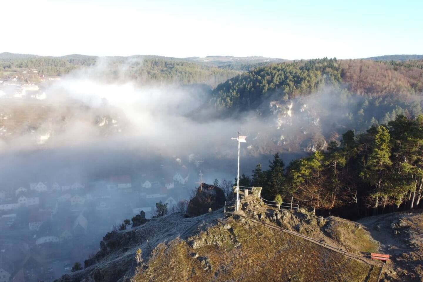 Un paysage montagneux offrant une vue dégagée sur une ville située en contrebas, une station météorologique installée sur un promontoire rocheux et une voie ferrée traversant la vallée.