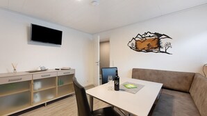 Une chambre moderne dotée d’une télévision à écran plat, d’une table à manger avec des chaises, d’un canapé et d’une œuvre d’art accrochée au mur.
