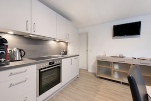Eine moderne Küche mit weißen Schränken, einem eingebauten Backofen, einer Kaffeemaschine und einem flachbildfernseher an der Wand.