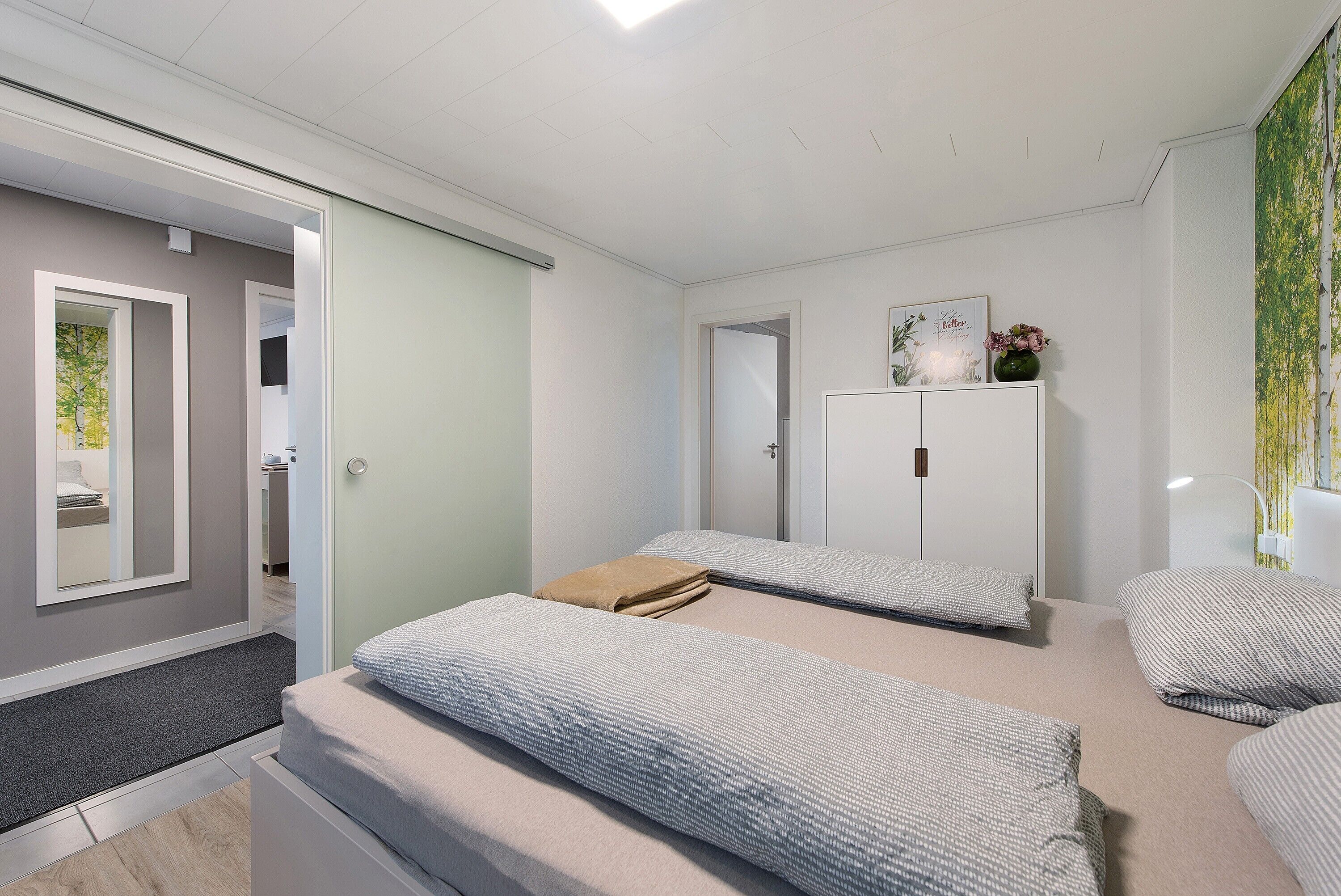 Ein modernes Schlafzimmer mit zwei Betten, einem Kleiderschrank und einem Spiegel.
