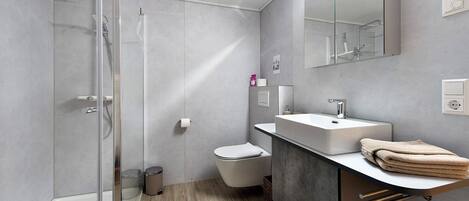 A modern bathroom with a glass shower enclosure, a toilet, a sink with a mirror, and a towel rack.