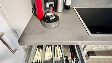 A kitchen with a coffee maker, a bottle, and utensils in a drawer.