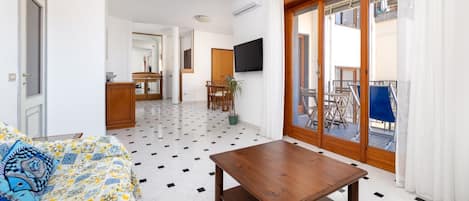 Une chambre d’hôtel comprenant un lit, une table en bois, une télévision, un coin repas et un balcon avec des chaises.