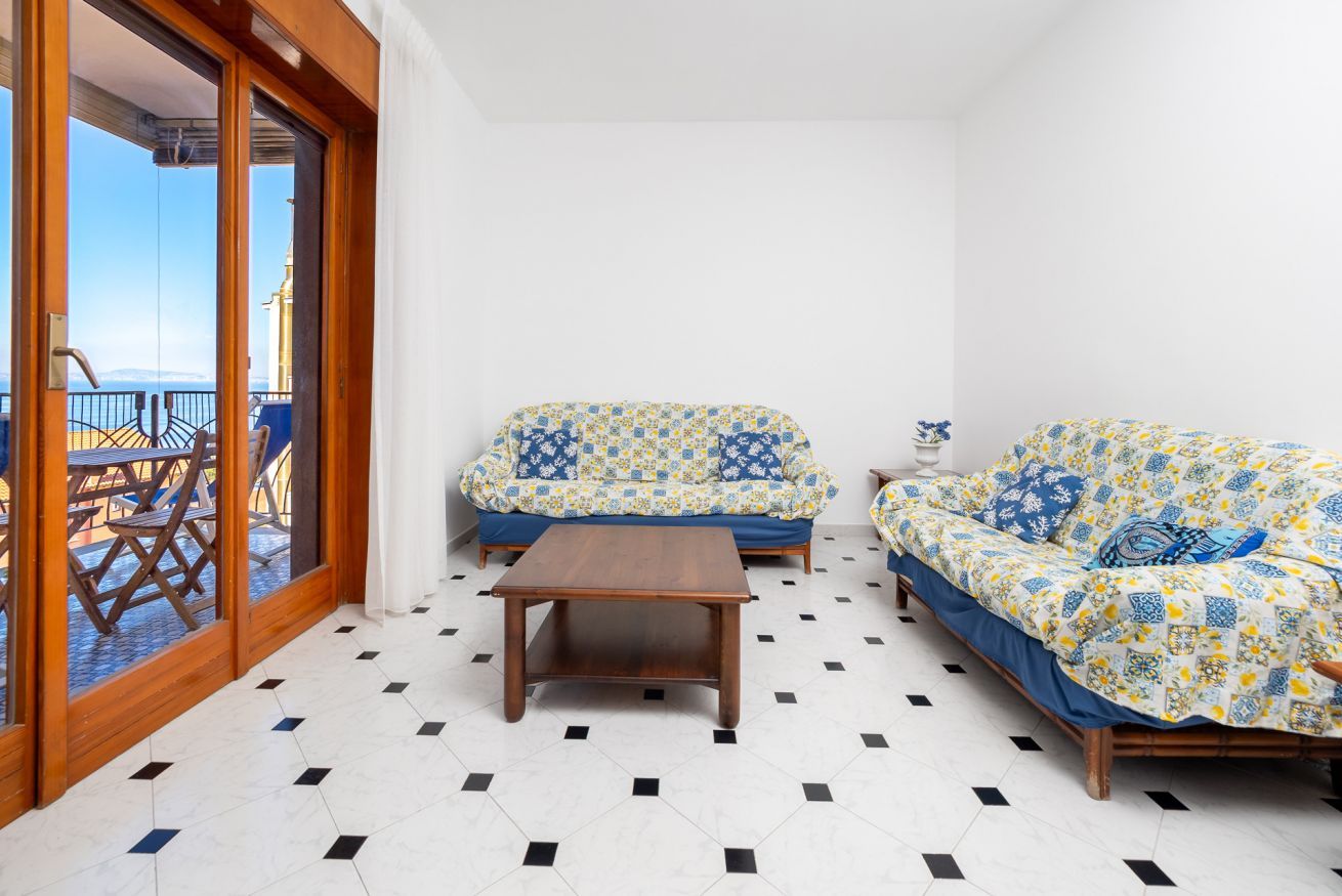 Una habitación con dos sofás, una mesa de madera y vista al mar a través de un ventanal.