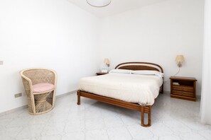A bedroom with a wooden bed, a wicker chair, a nightstand, and a wall-mounted lamp. - Capo Sereno - Large & Bright apt with terrace (Sorrento)