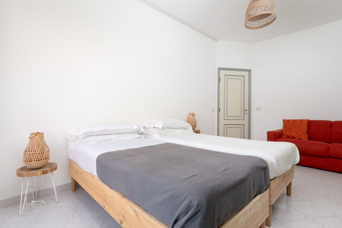 Een slaapkamer met een houten bed, witte wanden, een rode bank en een rieten lamp.