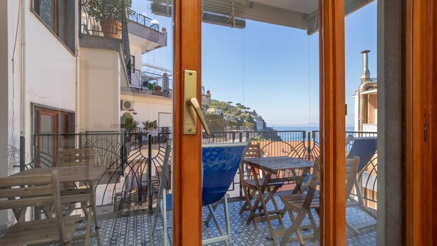 A balcony with a table and chairs, a blue chair, and a view of the sea. - Capo Sereno - Large & Bright apt with terrace (Sorrento)